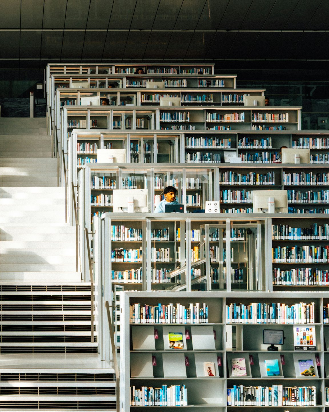 A man works on his laptop in a large modern library.