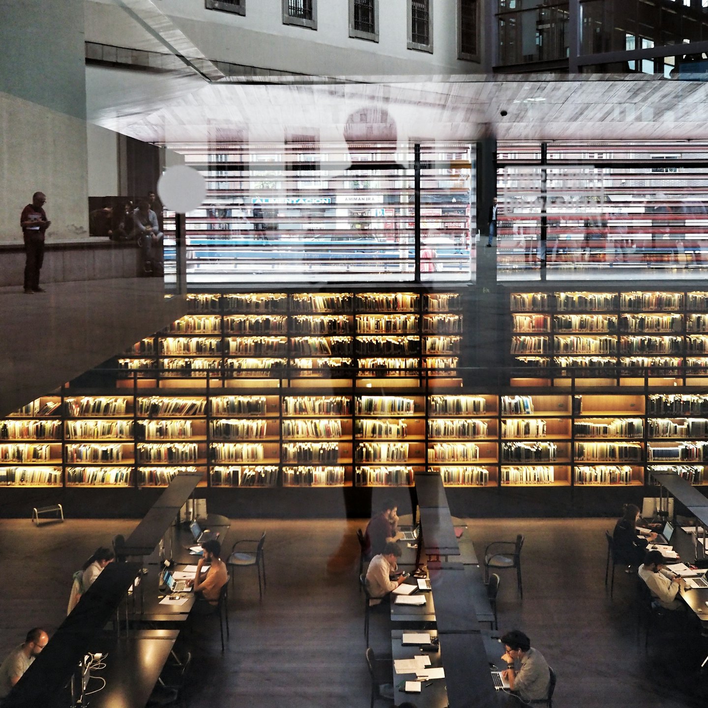 People studying and working in a modern library with many bookshelves.